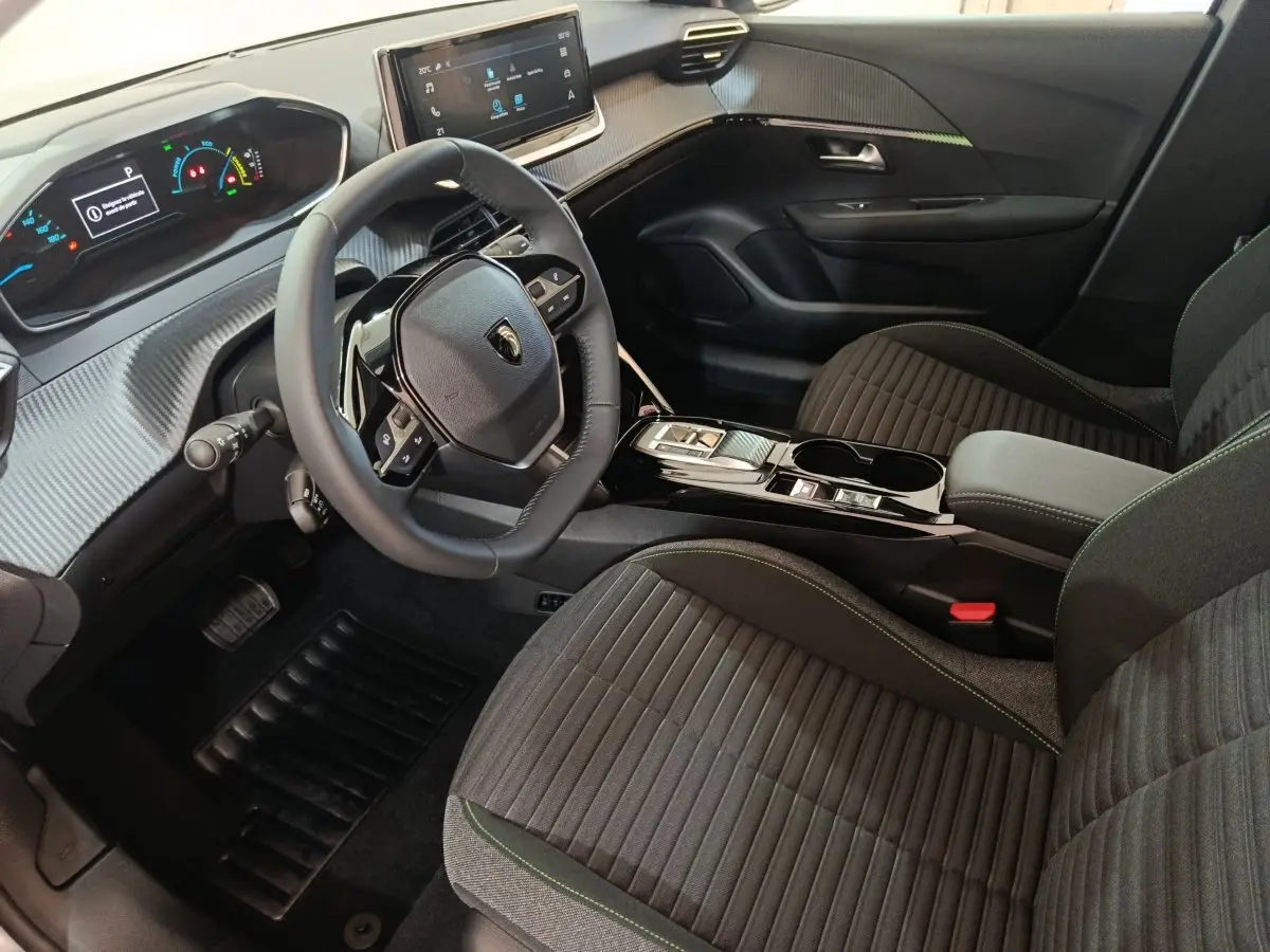 Intérieur de la Peugeot 208 électrique 2024, vue côté conducteur, volant cuir et tableau de bord digital.