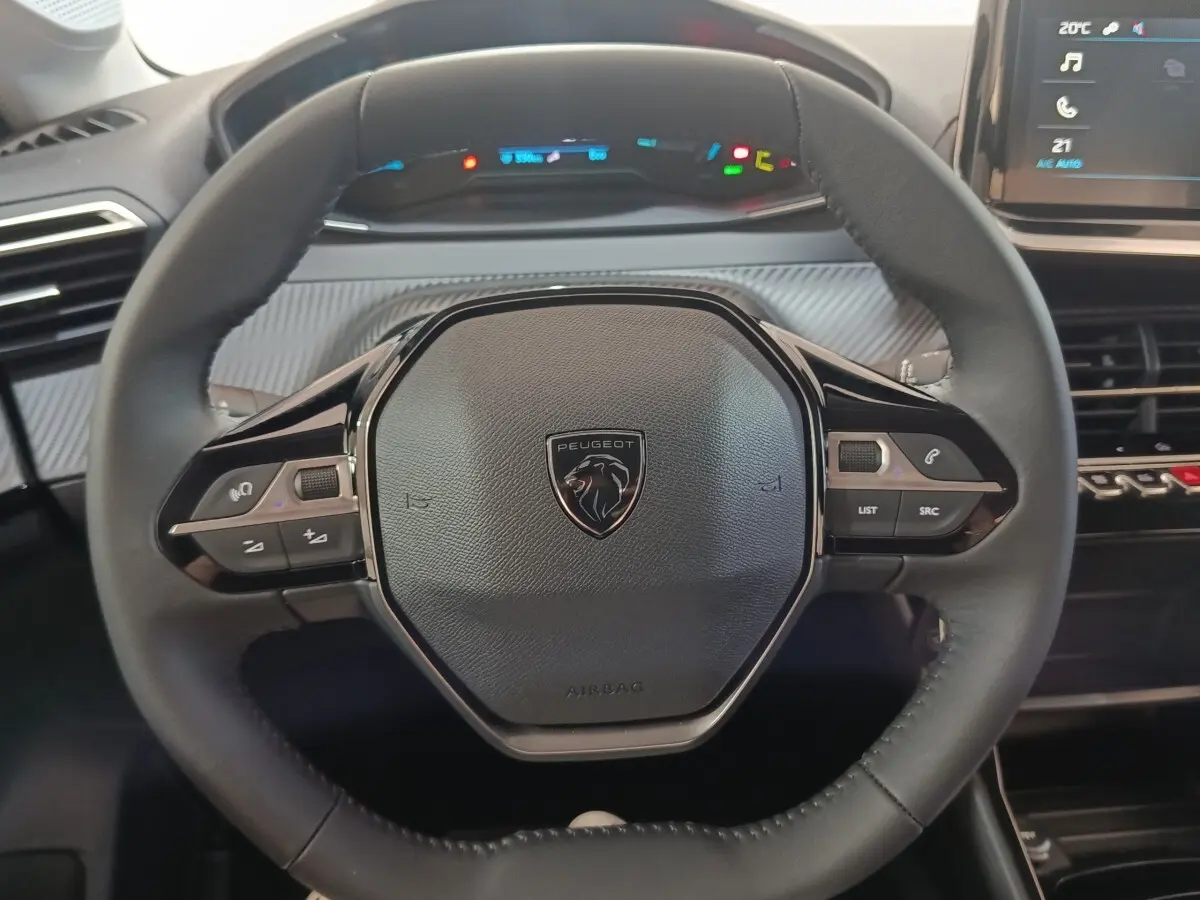Vue rapprochée du volant cuir multifonctions de la Peugeot 208 électrique 2024 avec tableau de bord numérique en arrière-plan.
