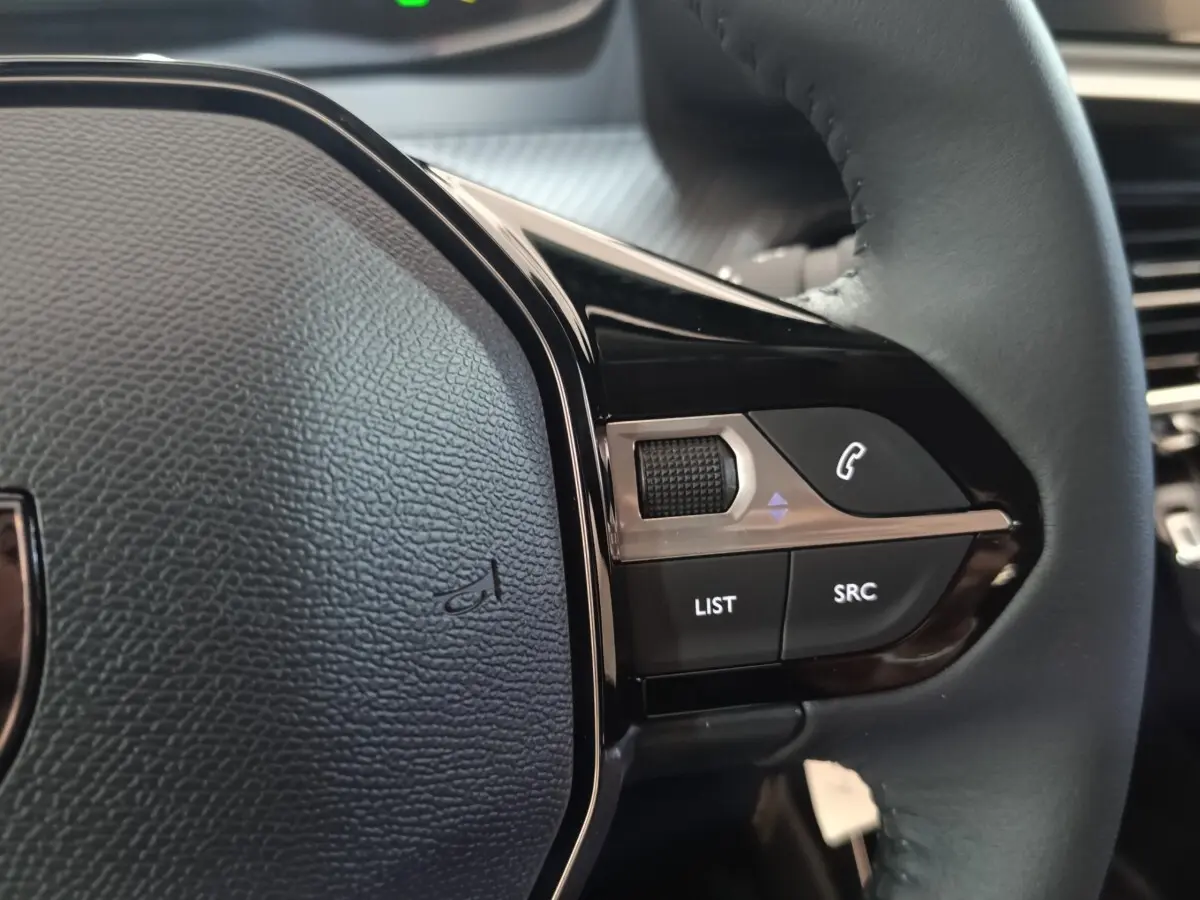 Gros plan sur les commandes multifonctions du volant cuir côté droit du Peugeot 208 électrique gris clair 2024.