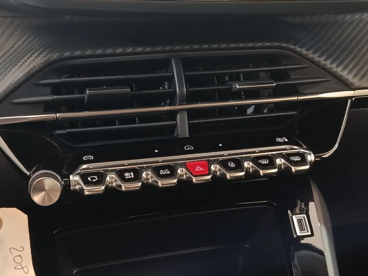 Gros plan sur la console centrale de la Peugeot 208 électrique 2024, boutons de commande et aérateurs noirs.