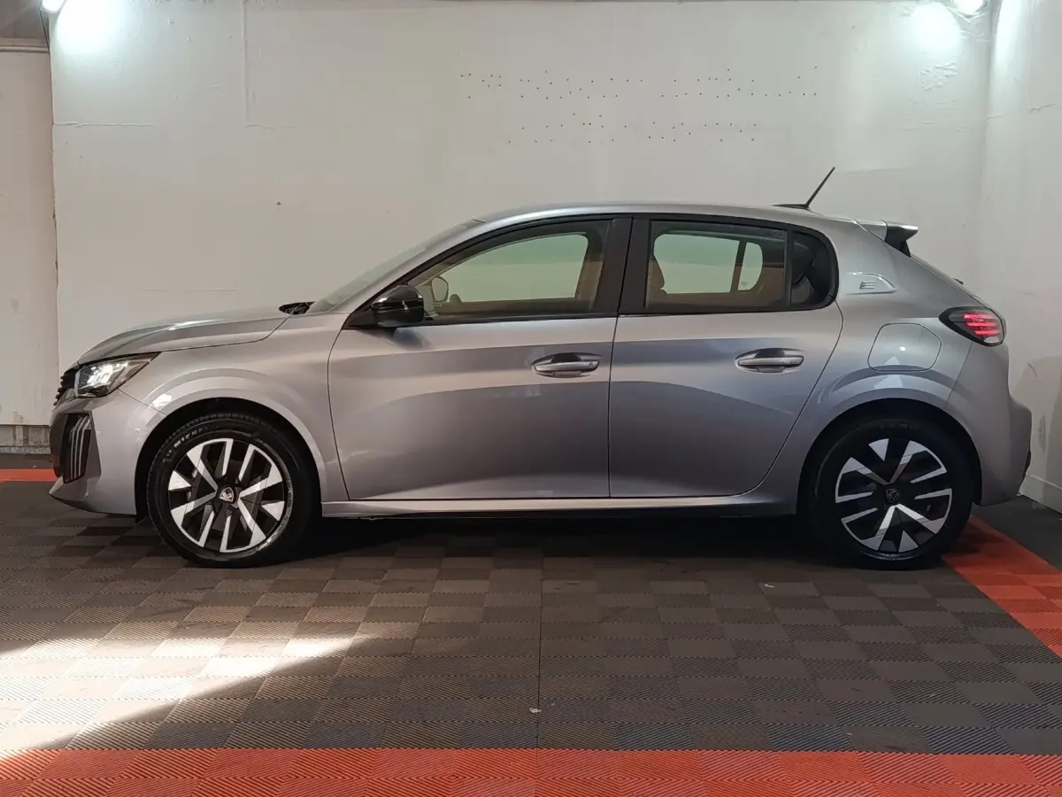 Peugeot 208 électrique gris clair vue de profil côté gauche dans un garage avec sol noir et rouge.