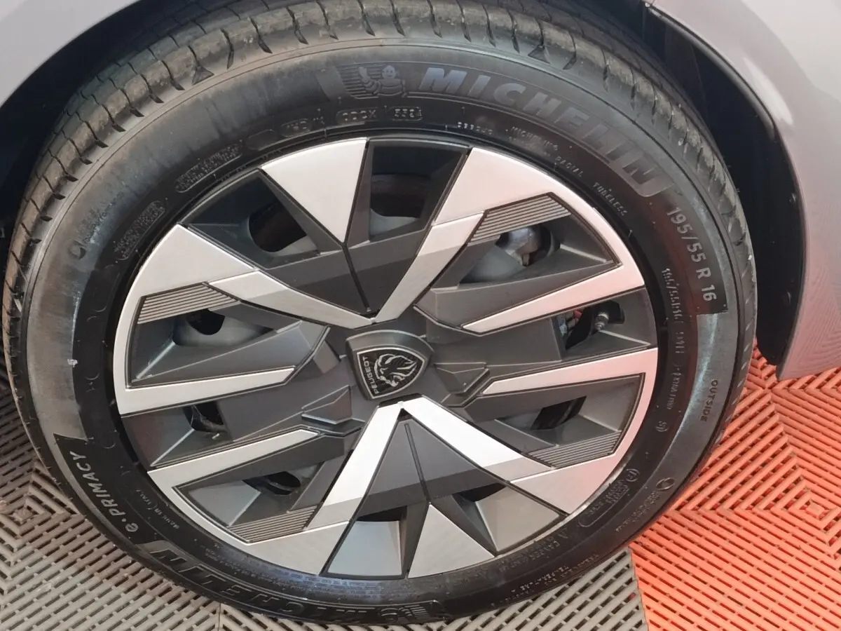 Gros plan sur la roue avant droite de la Peugeot 208 électrique gris clair avec jante au design géométrique noir et argent.