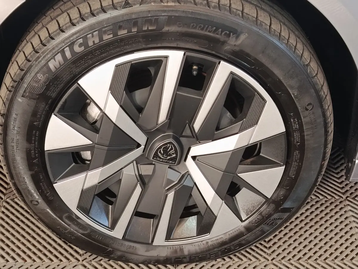 Gros plan sur la roue avant droite de la Peugeot 208 électrique 2024 gris clair avec jante au design géométrique bicolore.