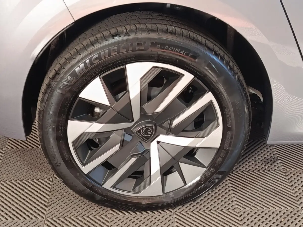 Gros plan sur la roue avant droite d’une Peugeot 208 électrique gris clair avec jante au design géométrique bicolore.