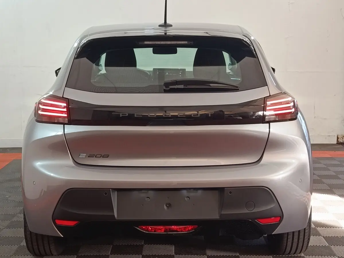 Vue arrière d'une Peugeot 208 électrique gris clair 2024 avec feux LED allumés et logo PEUGEOT central.