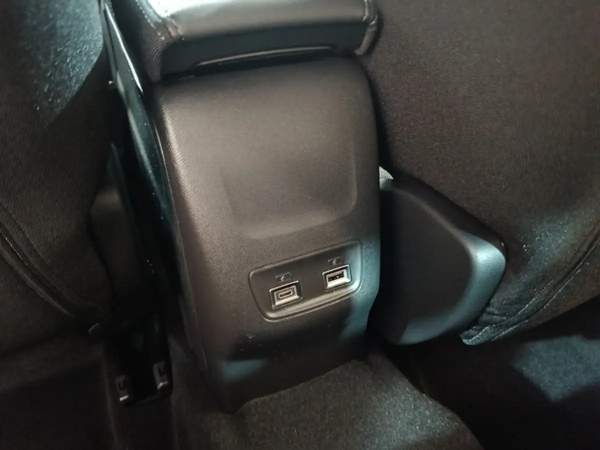 Vue rapprochée des ports USB arrière noirs entre les sièges arrière d'une Peugeot 208 électrique gris clair.