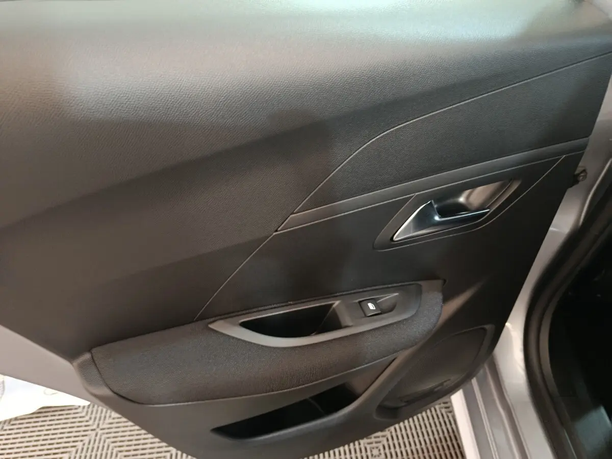 Vue intérieure côté droit de la porte d’une Peugeot 208 électrique 2024 gris clair avec poignée argentée et bouton de vitre.