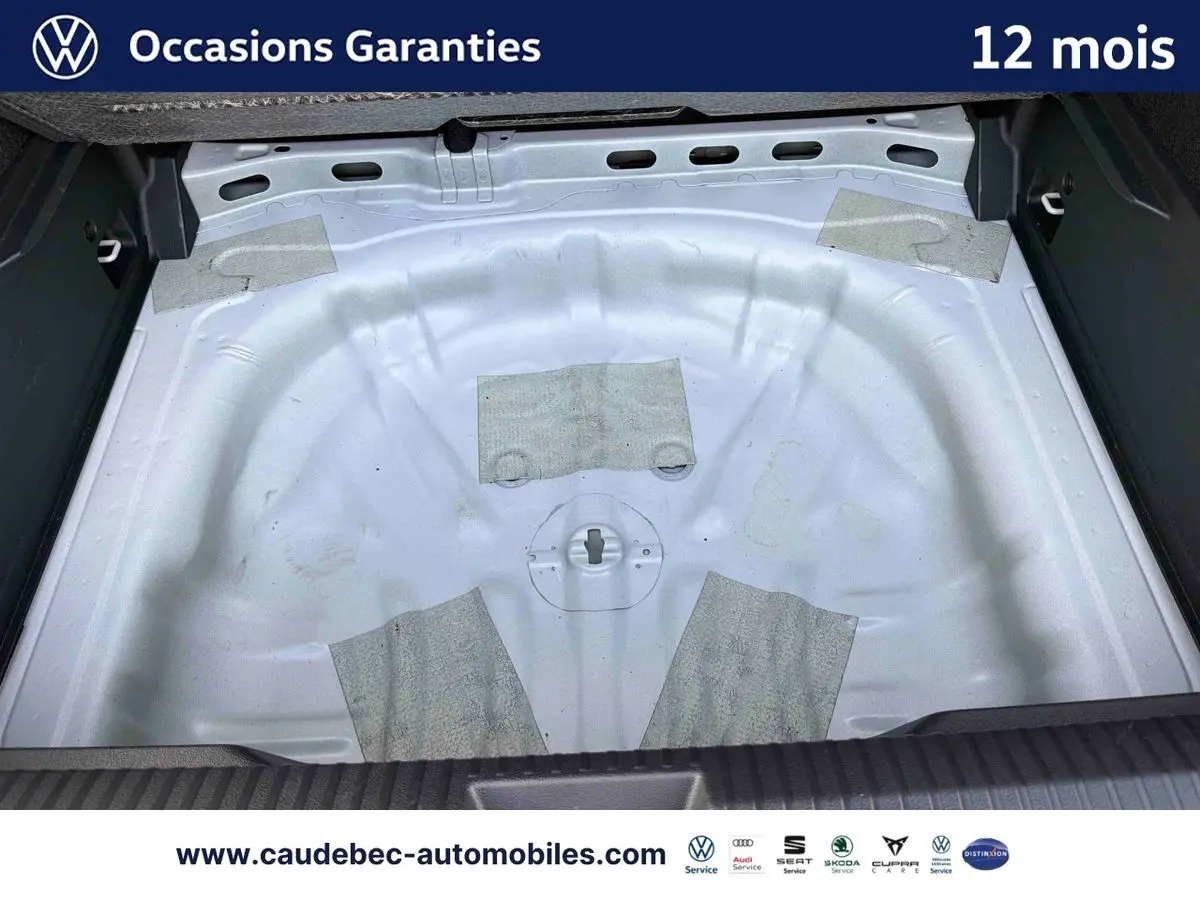 Coffre ouvert d’un Volkswagen T-Roc blanc, vue plongeante sur l’espace de rangement sans roue de secours.