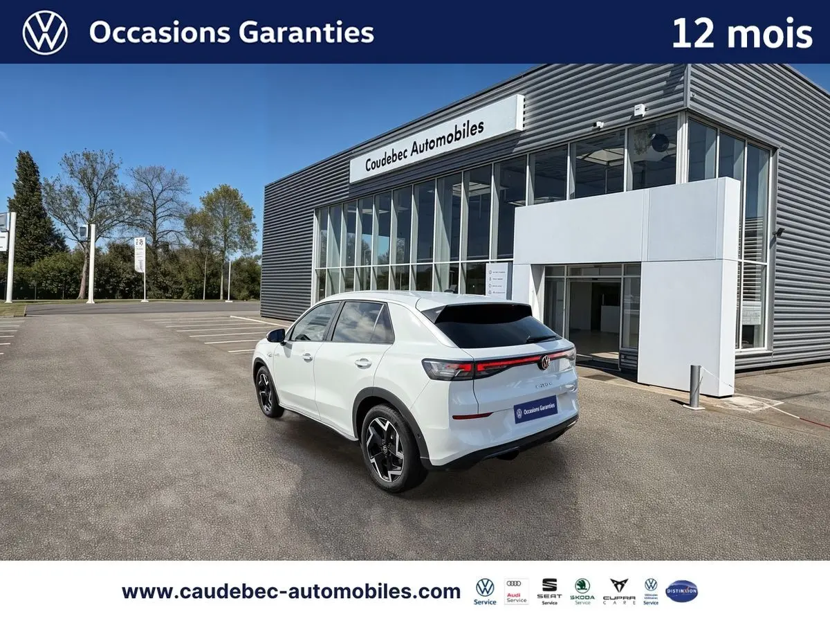 Volkswagen T-Roc blanc en 3/4 arrière droit, avec feux LED et jantes noires brillantes, devant un bâtiment moderne.