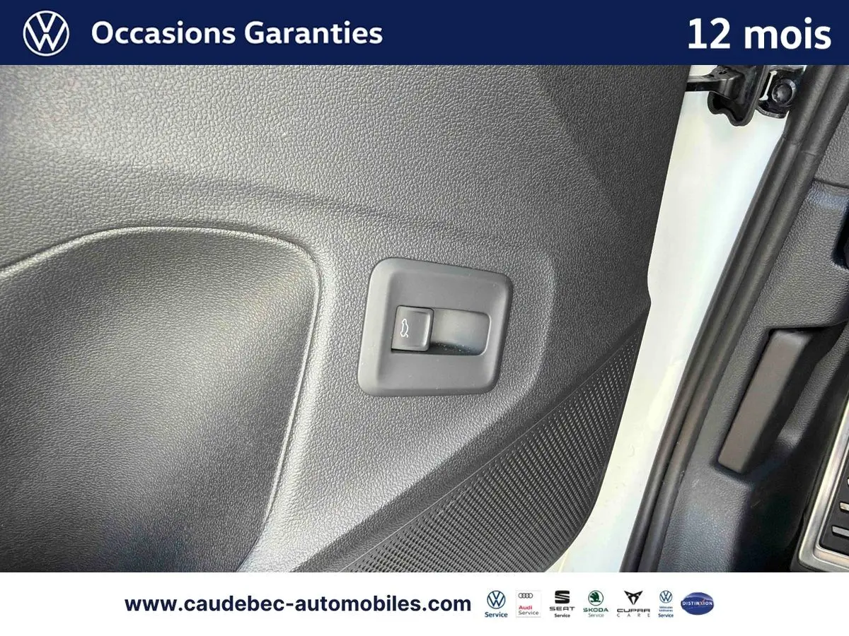 Gros plan sur le bouton d'ouverture du hayon dans l'encadrement de porte côté conducteur d'un Volkswagen T-Roc blanc.