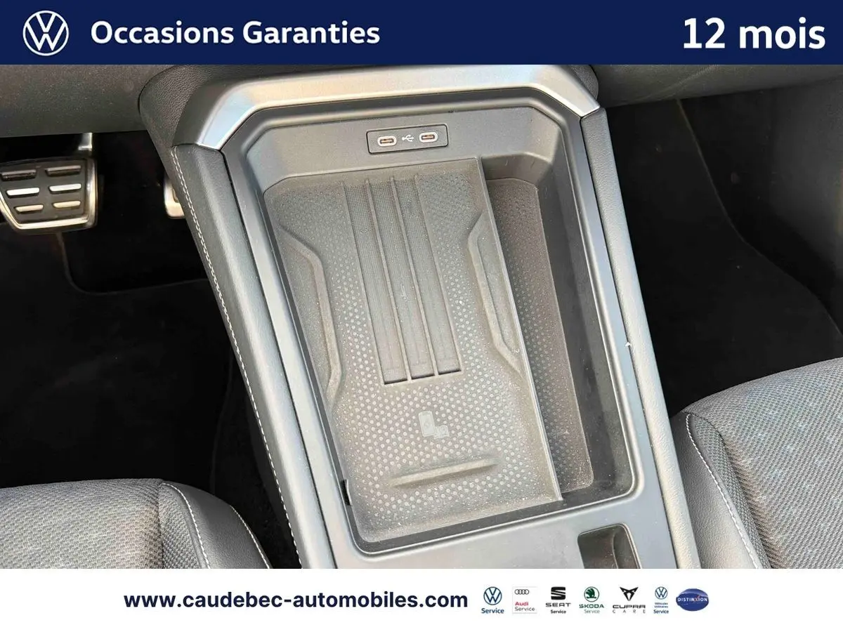 Vue rapprochée de la console centrale noire du Volkswagen T-Roc 2025 avec zone de recharge sans fil et ports USB.