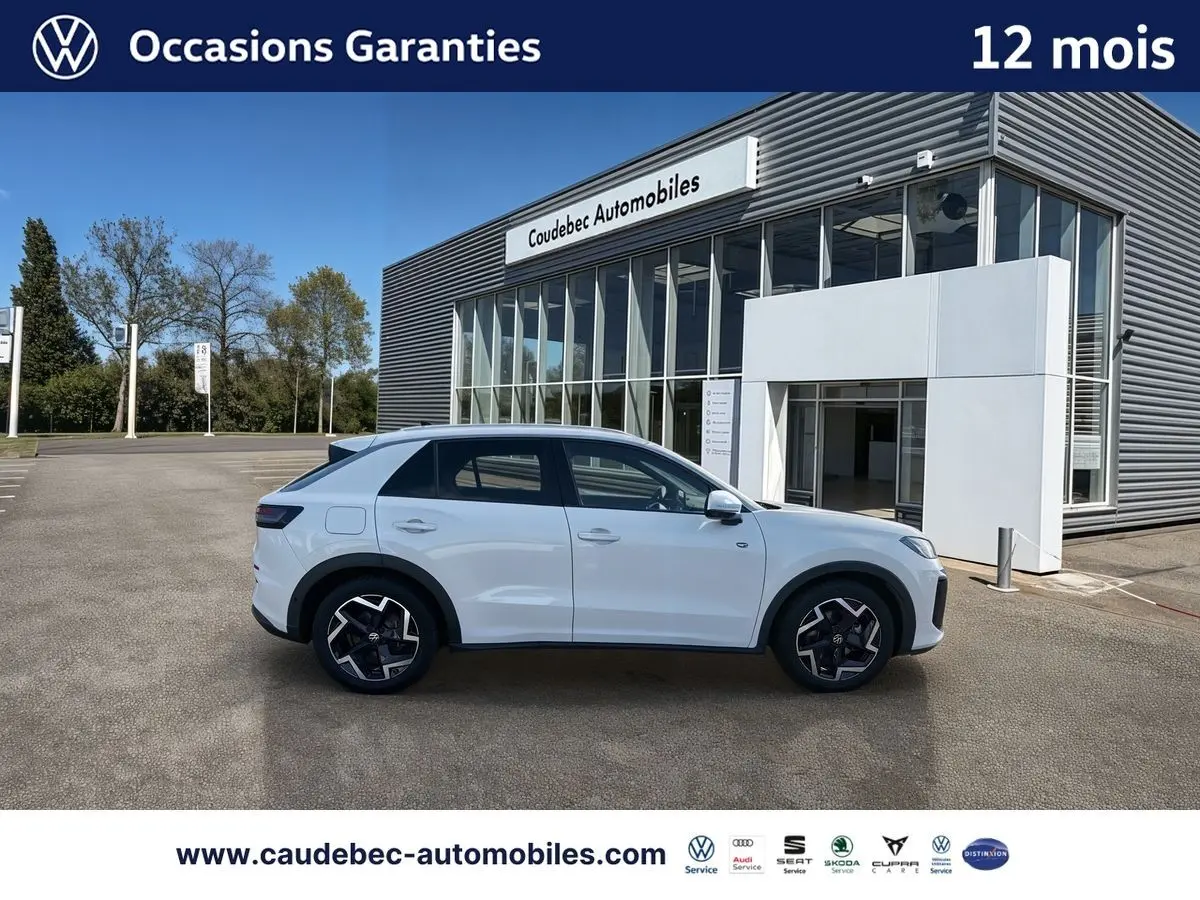 Volkswagen T-Roc blanc vue de profil côté gauche, avec jantes alliage noires et bâtiment Caudebec Automobiles en arrière-plan.