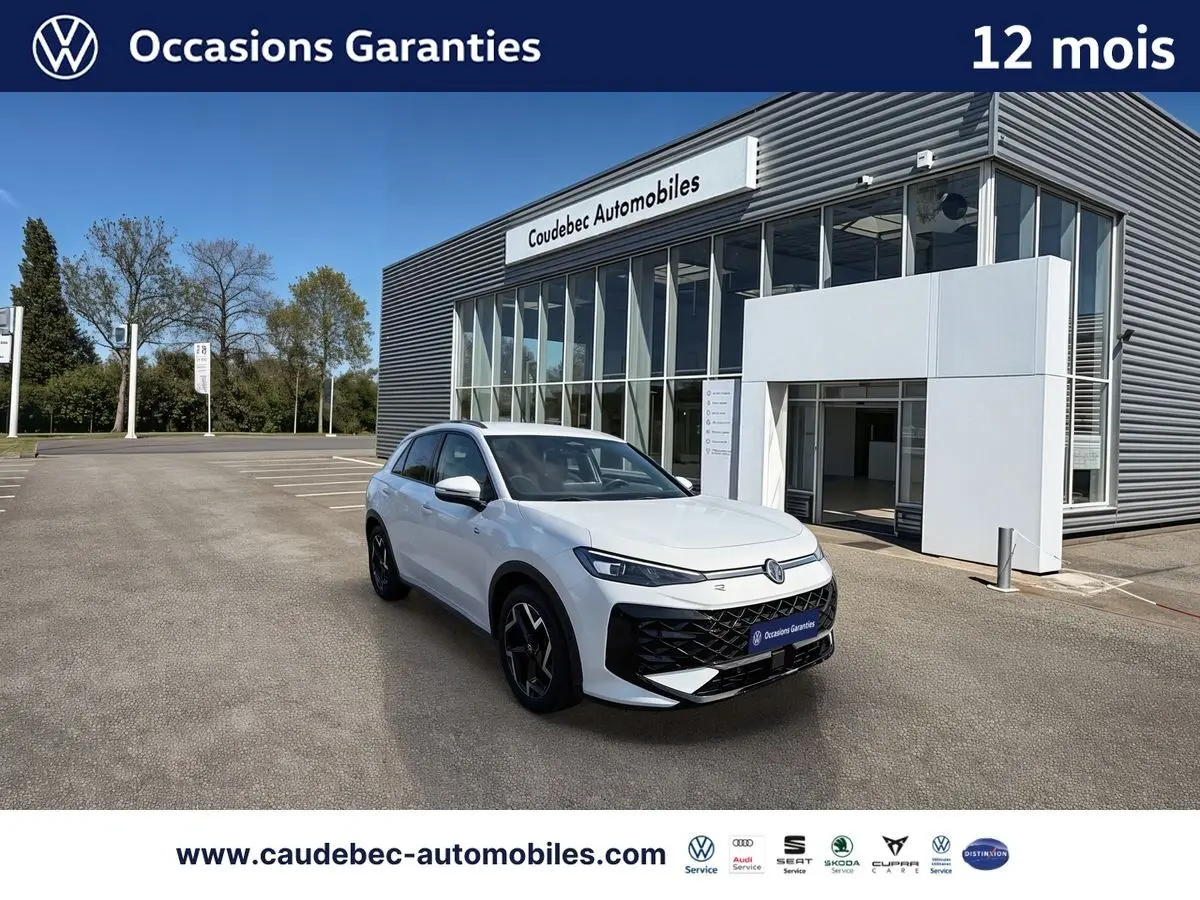 Volkswagen T-Roc blanc vue 3/4 avant droit, avec jantes noires et logo lumineux, devant un bâtiment moderne.