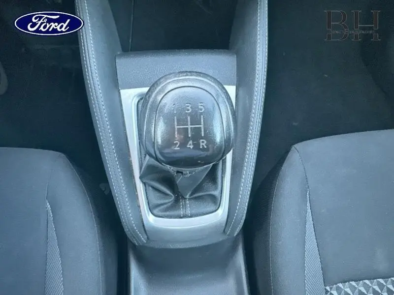 Gros plan sur levier de vitesses manuel noir et console centrale entre sièges tissu noir d'une Nissan Micra gris acier.