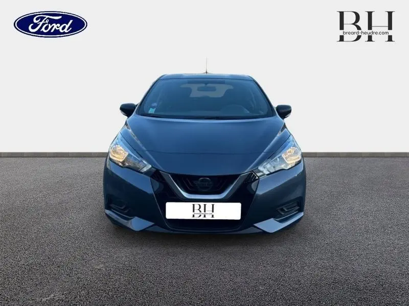 Vue frontale d'une Nissan Micra gris acier 2018 avec phares allumés sur fond neutre.