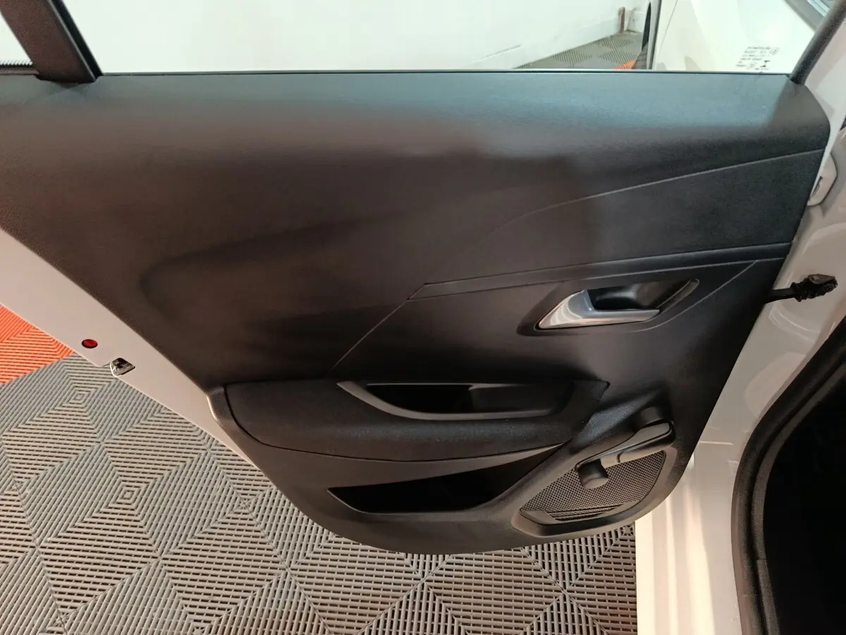 Vue intérieure de la porte arrière droite noire d'une Peugeot 208 électrique blanche, avec poignée et haut-parleur intégrés.