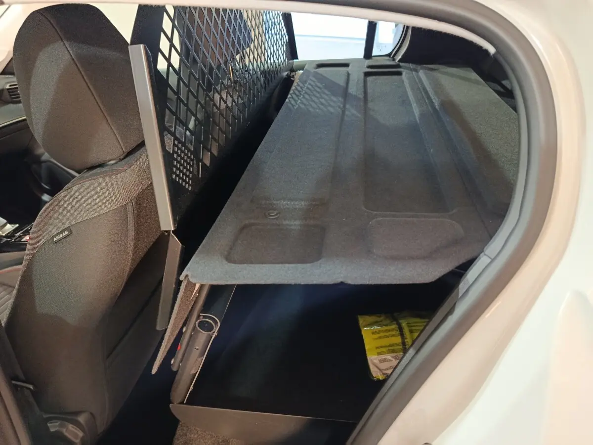 Vue intérieure côté droit du coffre de la Peugeot 208 électrique blanche avec tablette de coffre relevée et siège avant noir.