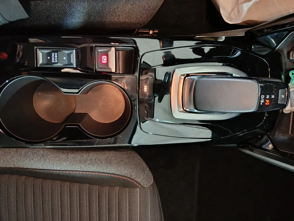 Vue plongeante sur la console centrale noire de la Peugeot 208 électrique avec levier de vitesses et boutons Drive Mode et frein à main.