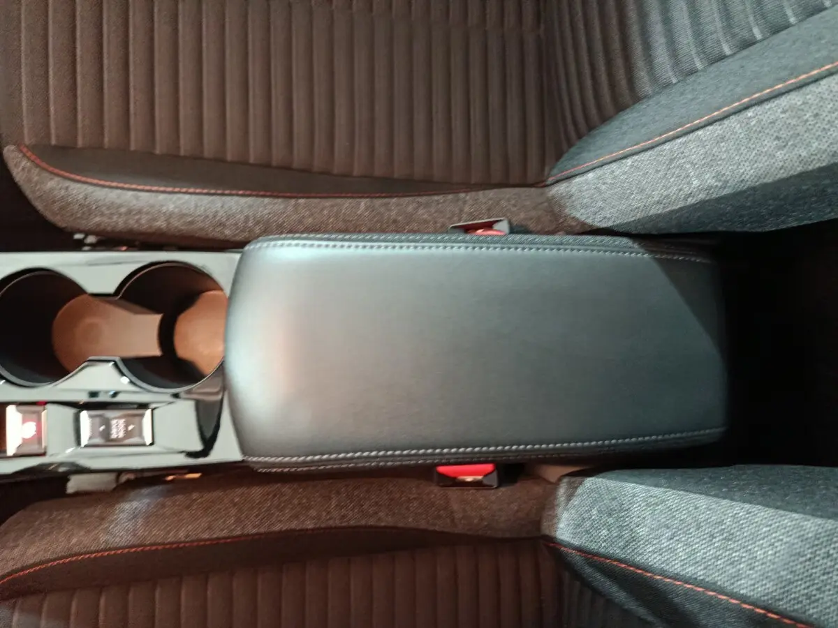 Vue plongeante sur l'accoudoir central noir et les sièges gris avec surpiqûres rouges de la Peugeot 208 Electrique Active Business.