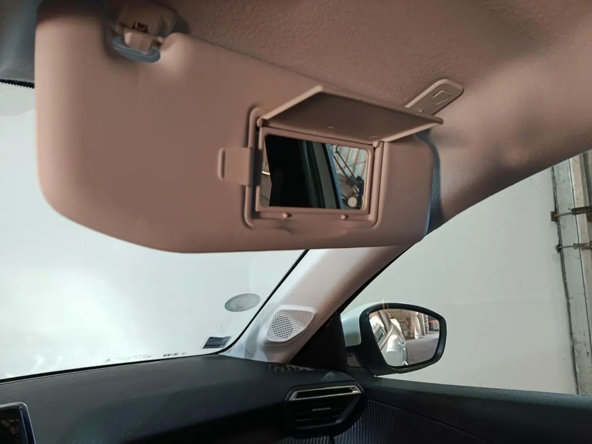 Intérieur de la Peugeot 208 électrique blanc, vue côté passager avec pare-soleil et miroir de courtoisie ouvert.