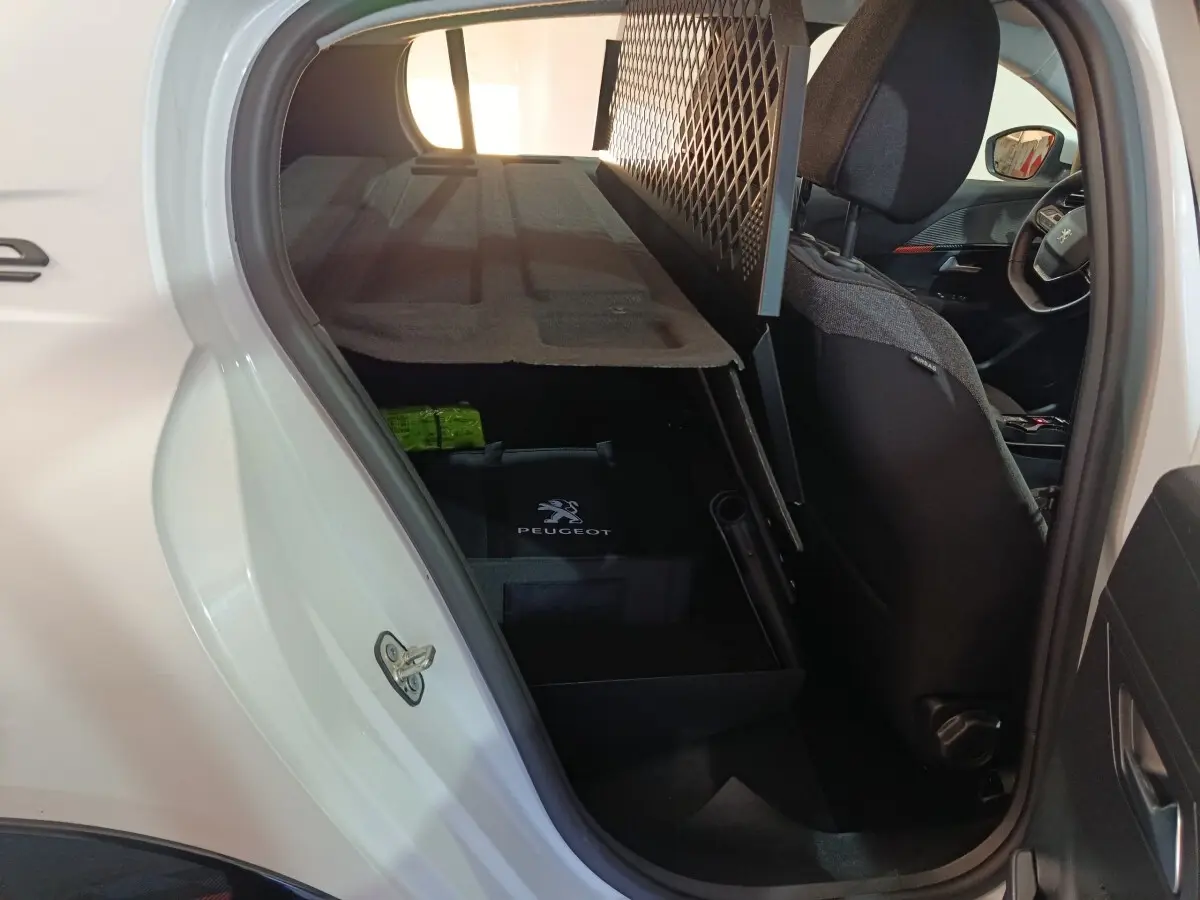 Vue intérieure côté gauche arrière d’une Peugeot 208 électrique blanche, avec siège avant et filet de protection visible.