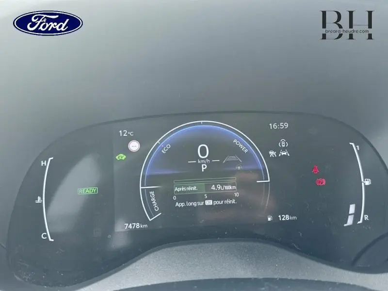 Tableau de bord numérique d'une Toyota Yaris Cross blanc, affichant la consommation et l'autonomie, vu de face.