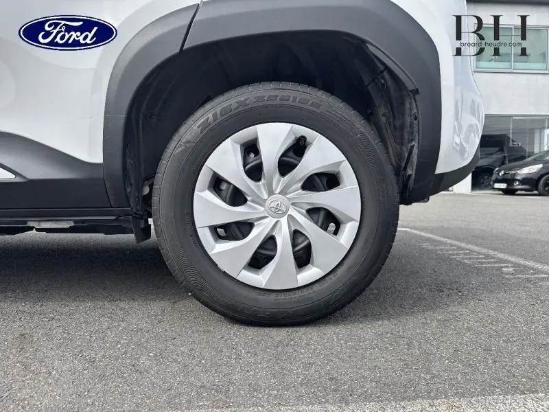 Gros plan sur la roue avant droite d'une Toyota Yaris Cross blanche avec enjoliveur argenté et pneus noirs.