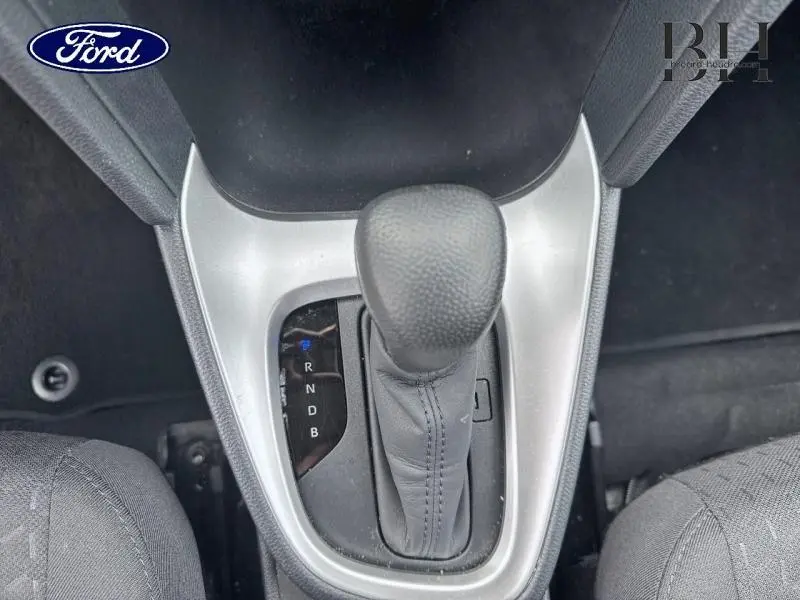 Le levier de vitesses automatique en cuir noir vu de dessus, entouré d'une console argentée et sièges en tissu gris.