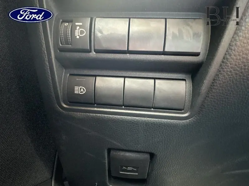 Gros plan sur les commandes d'éclairage et réglages intérieurs noirs d'un Toyota Yaris Cross blanc, vue côté conducteur.