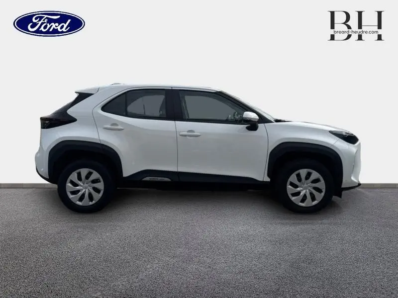 Profil droit d'un Toyota Yaris Cross blanc avec arches de roues noires et jantes à enjoliveurs, sur fond neutre.