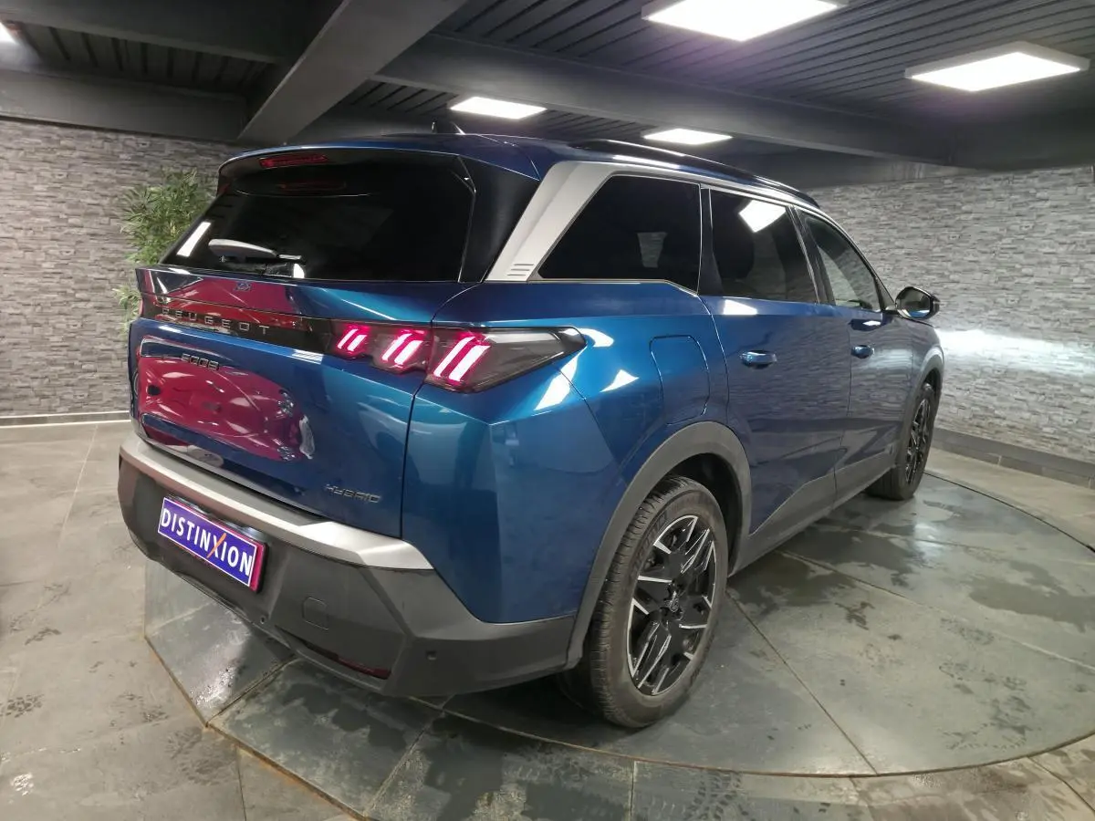 Vue 3/4 arrière droit d’un Peugeot 5008 bleu métallisé avec feux arrière à LED en forme de griffes et jantes alliage noires.