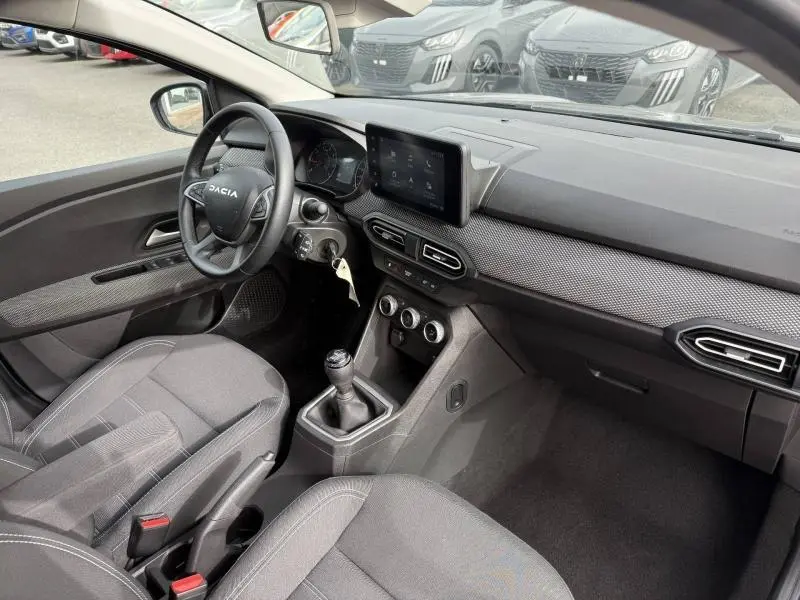 Vue intérieure côté conducteur du Dacia Jogger 2025, montrant le tableau de bord moderne avec écran tactile et levier de vitesses manuel.