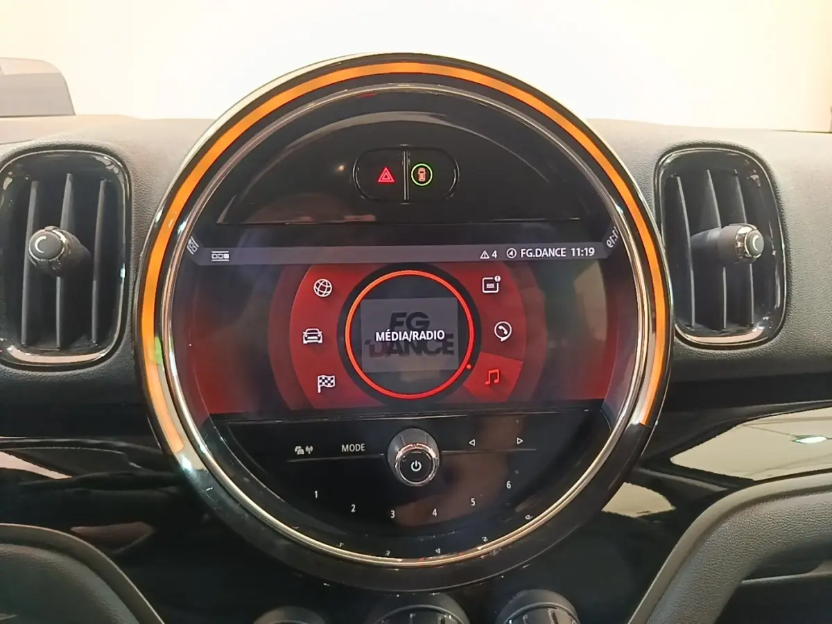 Vue rapprochée du tableau de bord de la MINI Countryman gris clair, avec écran tactile circulaire et éclairage orange.