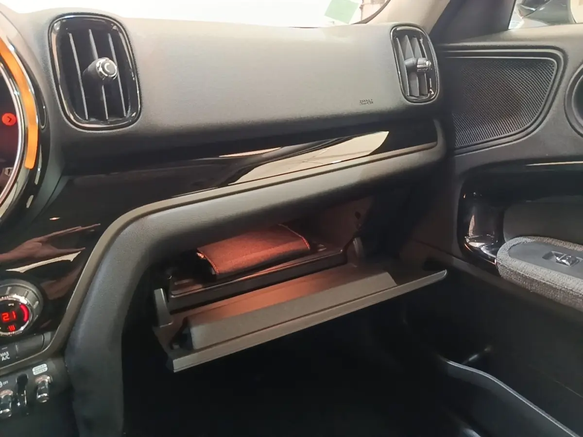 Intérieur MINI Countryman Cooper SE 2021, vue côté passager sur boîte à gants ouverte et tableau de bord noir.