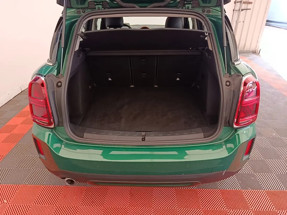 Vue arrière du coffre ouvert d'un MINI Countryman vert foncé avec tapis noir et feux arrière rouges.