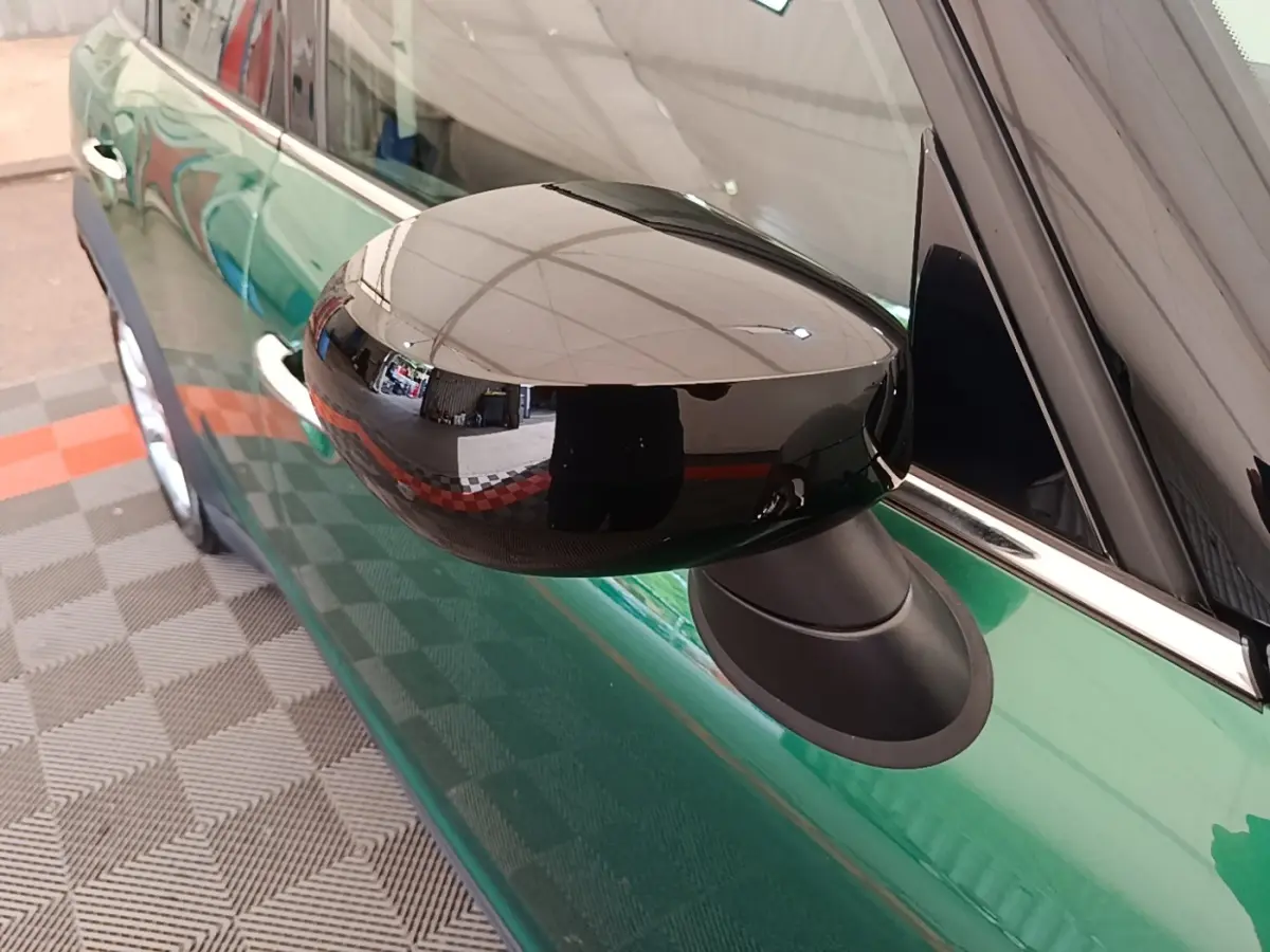 Gros plan sur le rétroviseur noir brillant côté gauche d'une MINI Countryman vert foncé, avec reflet net.
