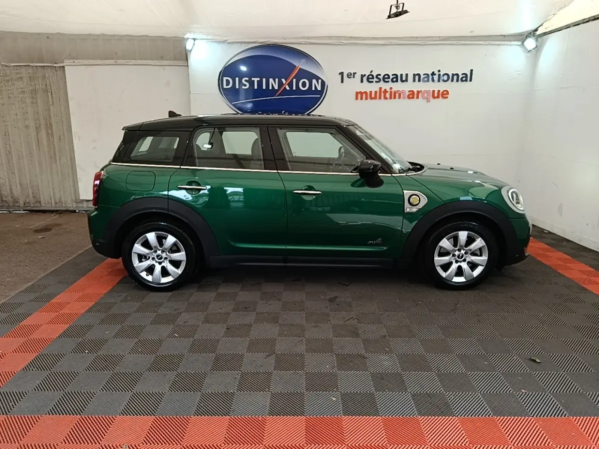 Vue de profil côté gauche d'un MINI Countryman hybride rechargeable vert foncé avec toit noir en intérieur showroom.