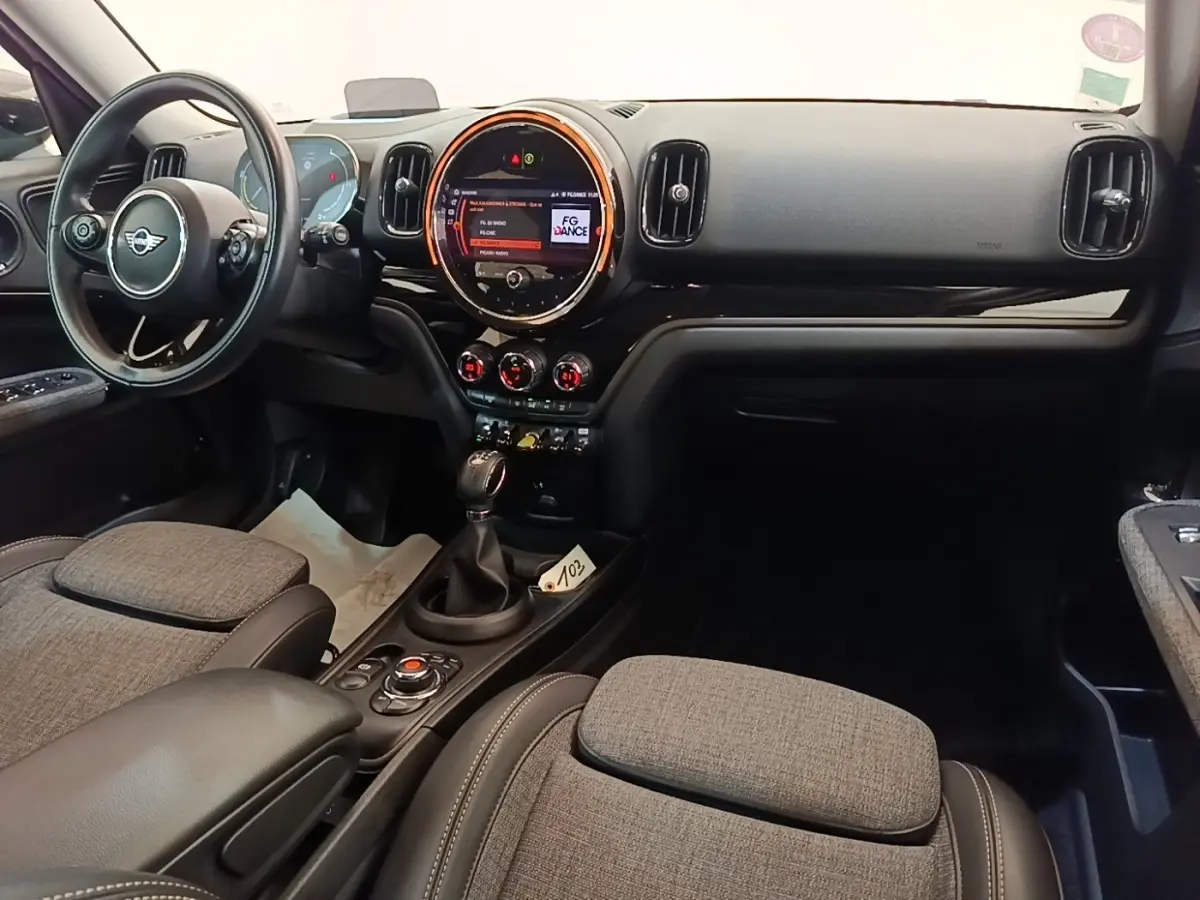 Vue intérieure avant du MINI Countryman Cooper SE, tableau de bord noir avec écran tactile rond et sièges tissu gris.