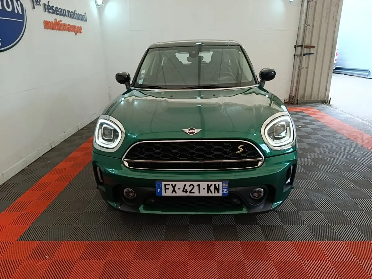 Vue avant d'une MINI Countryman Cooper SE hybride rechargeable en vert métallisé avec phares LED allumés.