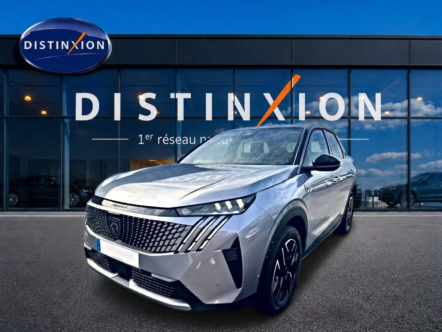 Peugeot 3008 gris artense en 3/4 avant droit, avec calandre distinctive et phares LED allumés, devant un showroom Distinxion.