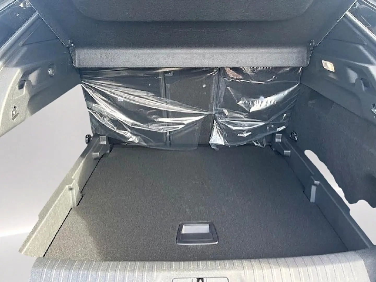 Vue intérieure du coffre spacieux du Peugeot 3008 gris Artense, avec banquette arrière protégée par un film plastique.