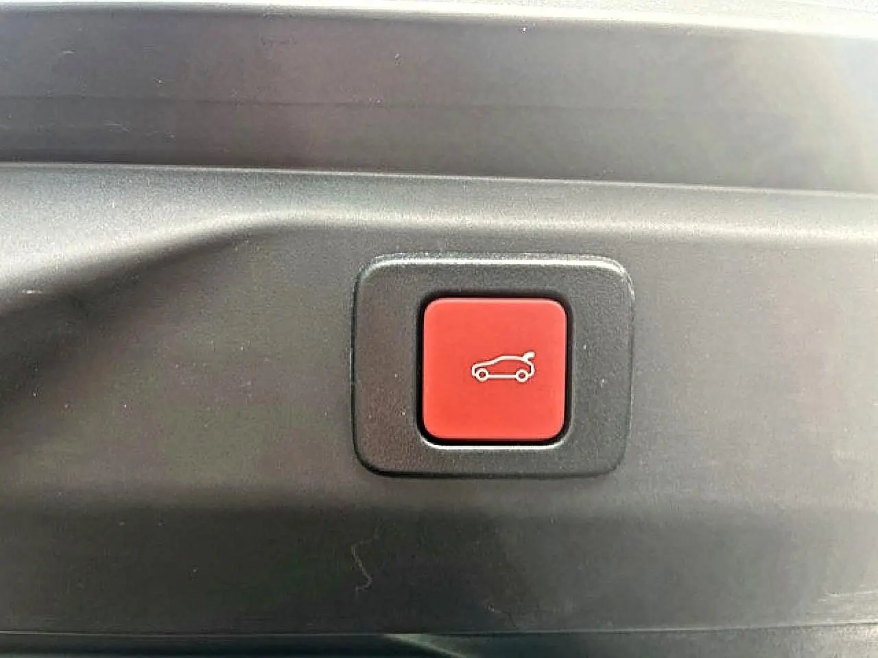Gros plan sur le bouton rouge d'ouverture électrique du coffre du Peugeot 3008 gris Artense, intérieur coffre visible.