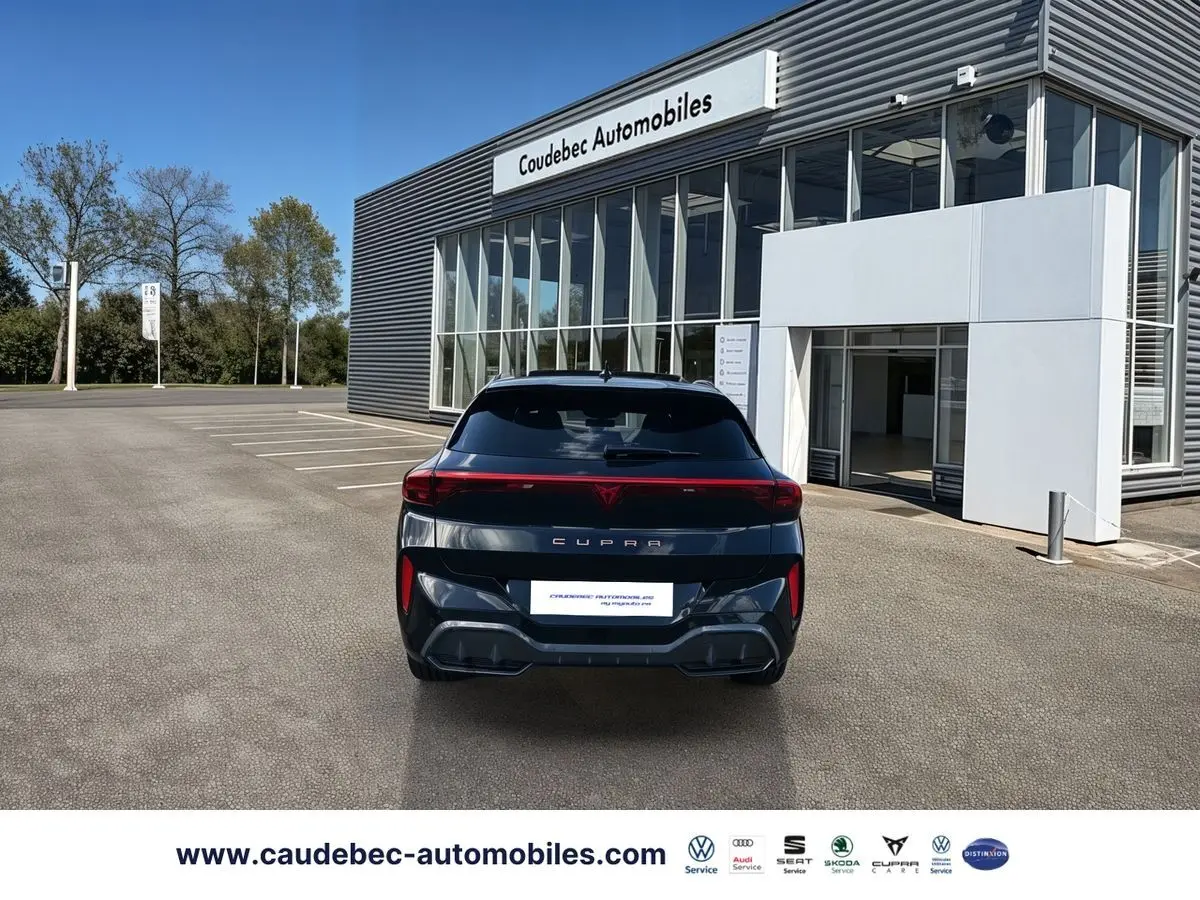 Vue arrière d'une CUPRA Terramar noire 2024, avec feux arrière continus et logo CUPRA lumineux, devant un bâtiment moderne.