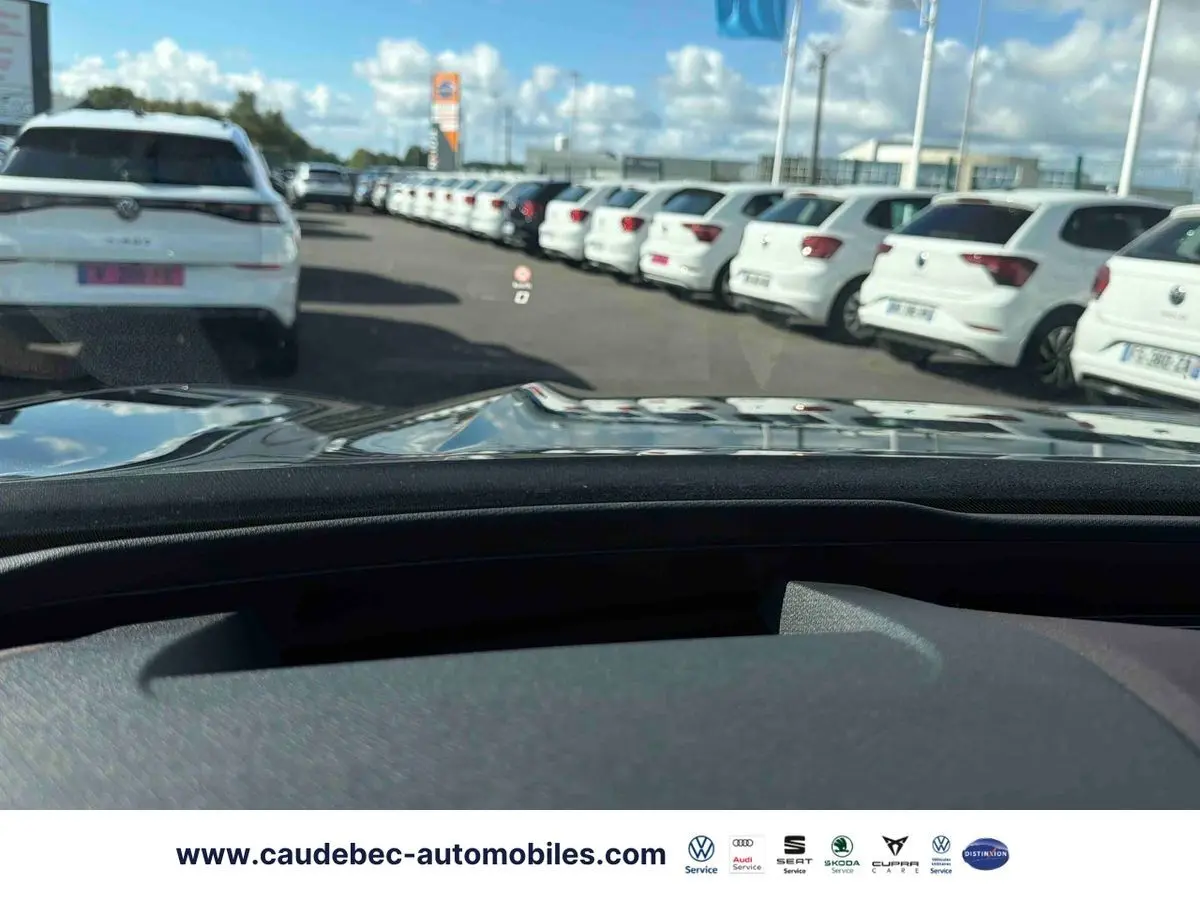 Vue depuis l’habitacle d’une CUPRA TERRAMAR noire, avec le capot et un parking de voitures blanches en arrière-plan.