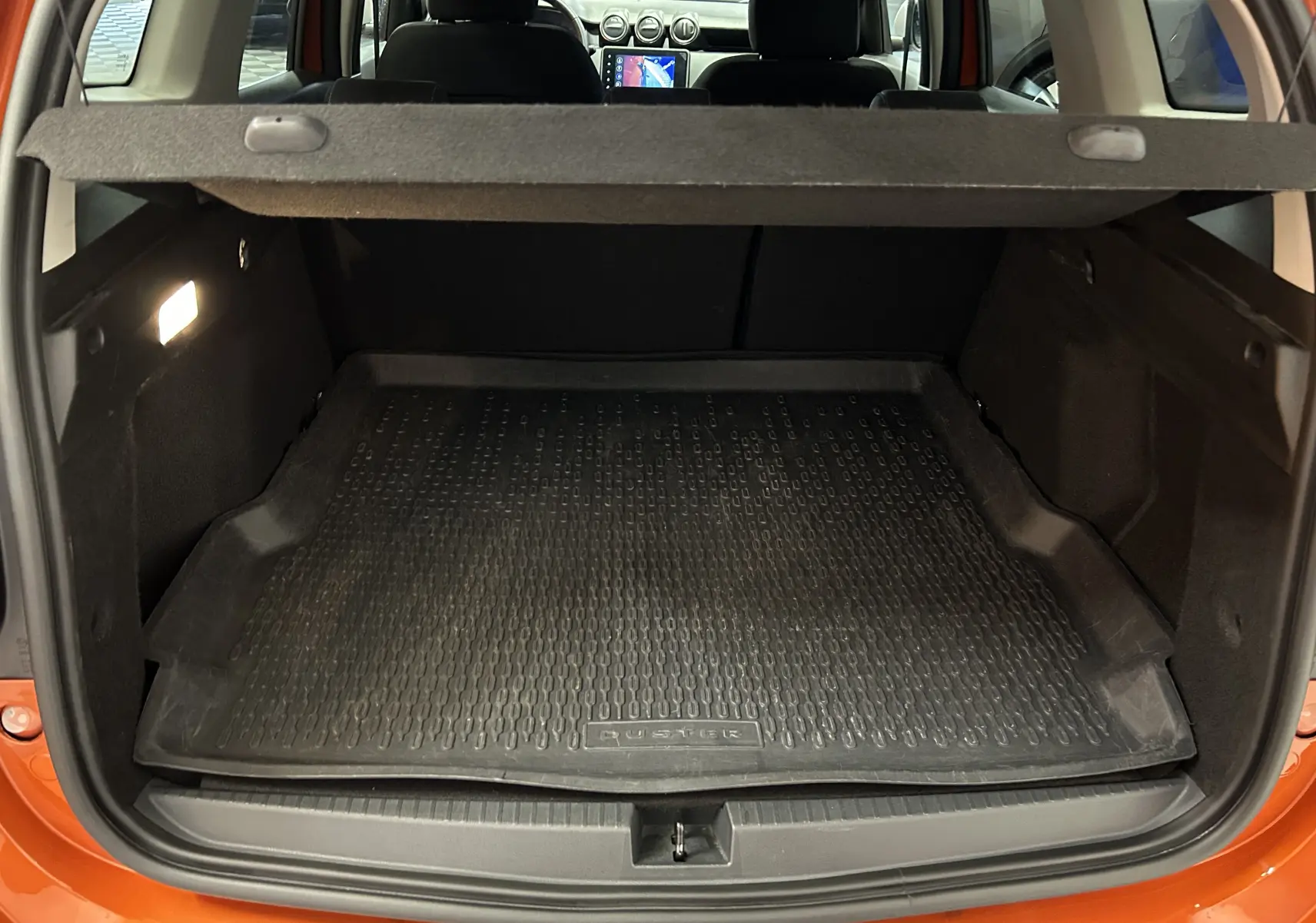 Coffre ouvert vu de l'arrière d'un Dacia Duster orange Arizona 2022 avec tapis de coffre en caoutchouc noir.