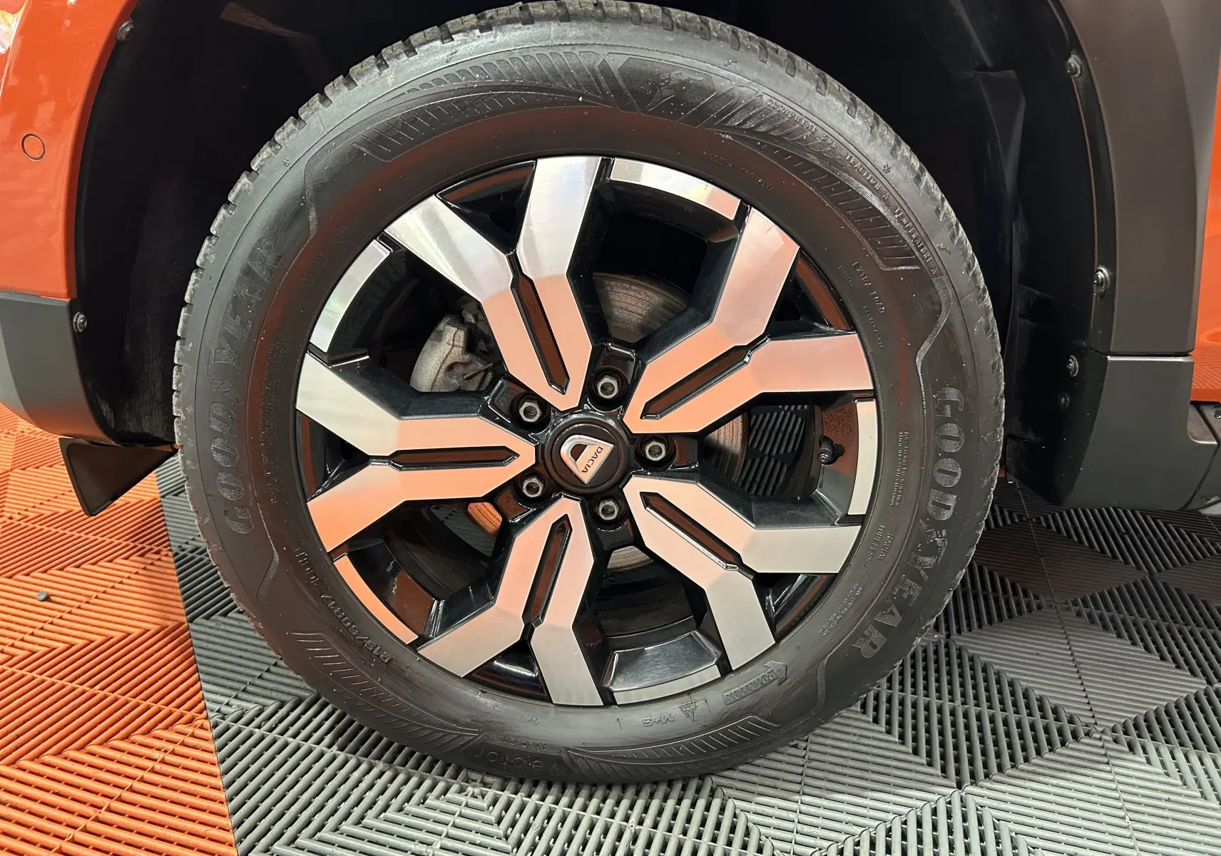 Gros plan sur la roue avant droite du Dacia Duster orange Arizona, avec jante alliage noir et argent et pneu Goodyear.