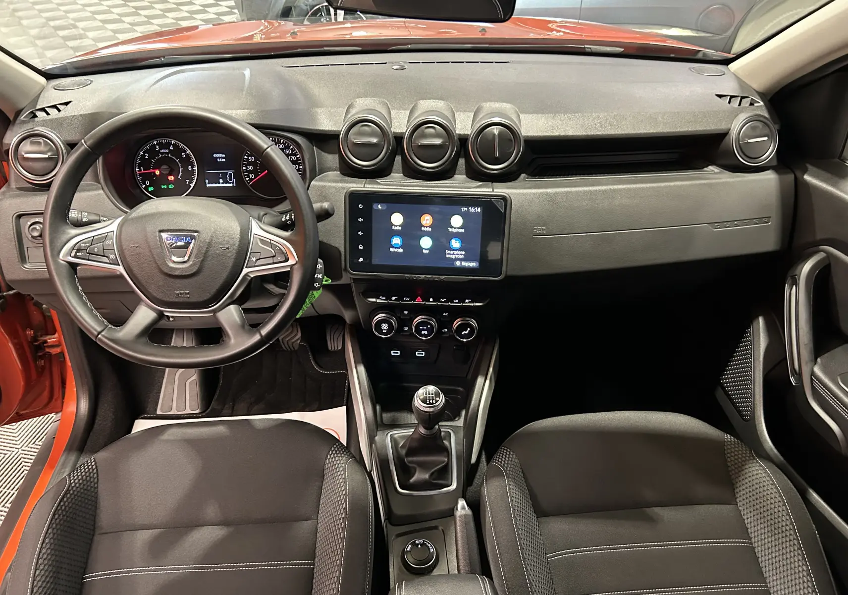 Vue intérieure avant du Dacia Duster 2022 orange Arizona, tableau de bord avec écran tactile et volant multifonction.