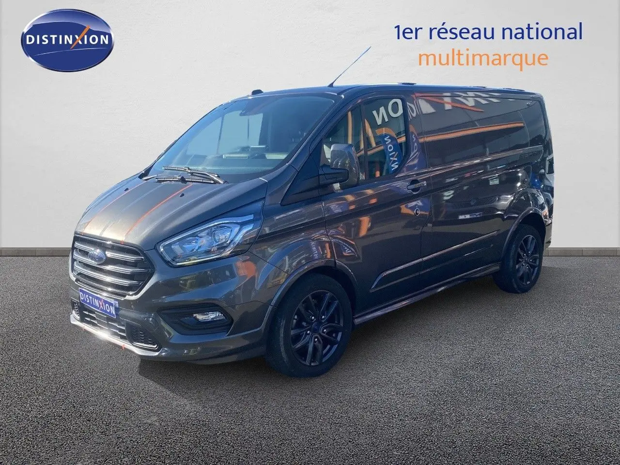Ford Transit Custom Fourgon gris magnetic en 3/4 avant droit, avec jantes noires et calandre chromée visible.