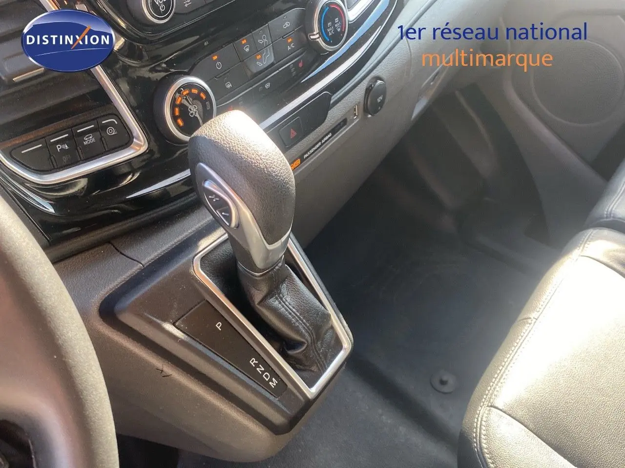 Gros plan sur la console centrale du Ford Transit Custom gris, mettant en valeur le levier de vitesse automatique et les commandes climatiques.