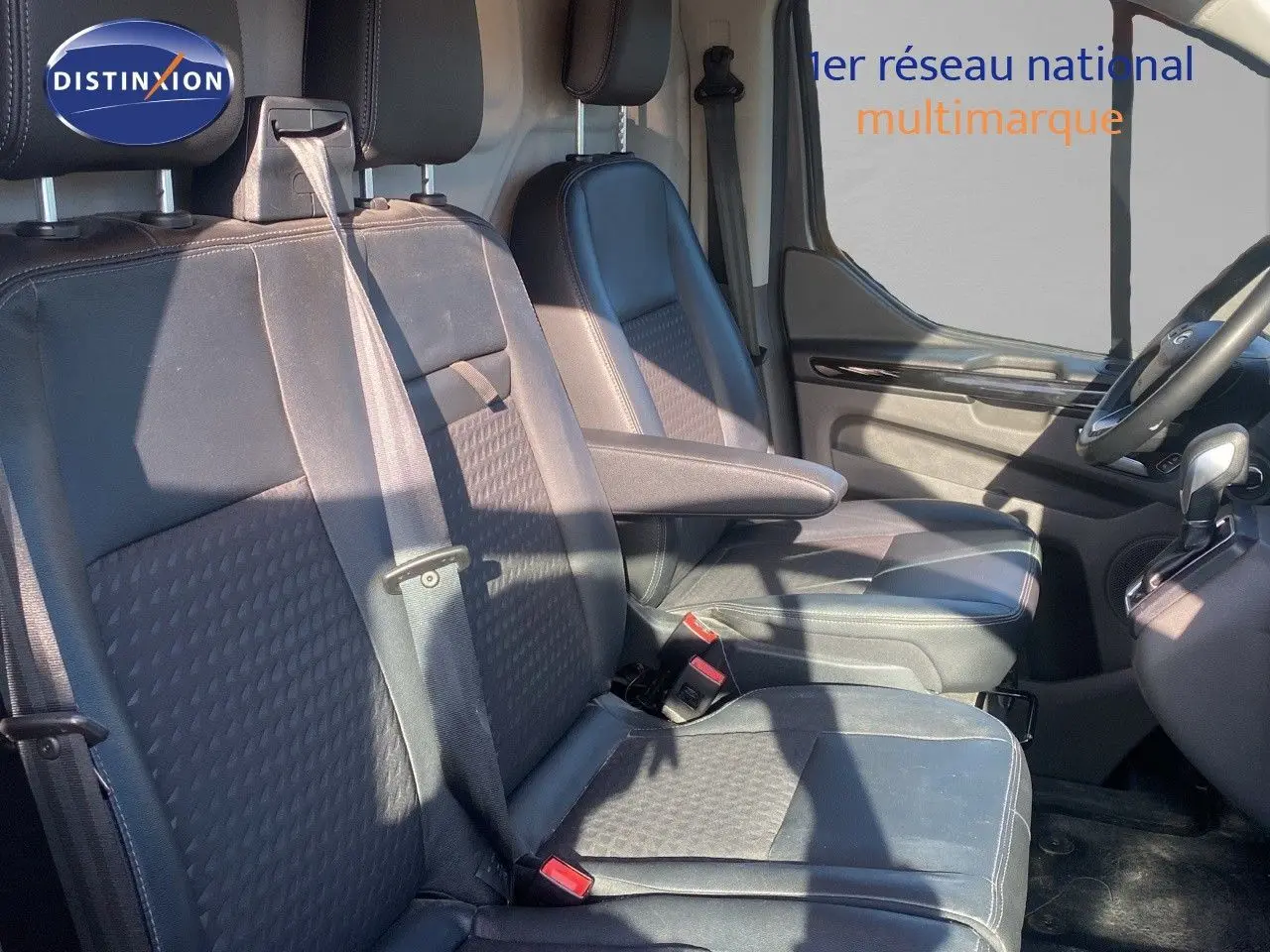 Intérieur du Ford Transit Custom gris magnetic, vue côté conducteur sur les sièges avant en cuir noir avec accoudoir.